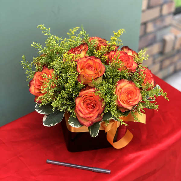 Orange roses in a black box with green filler and an orange ribbon