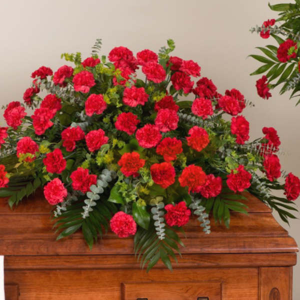 Large red carnation arrangement with greenery on a wooden casket