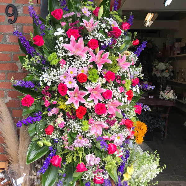 Large standing floral spray with pink lilies, red roses, and purple flowers
