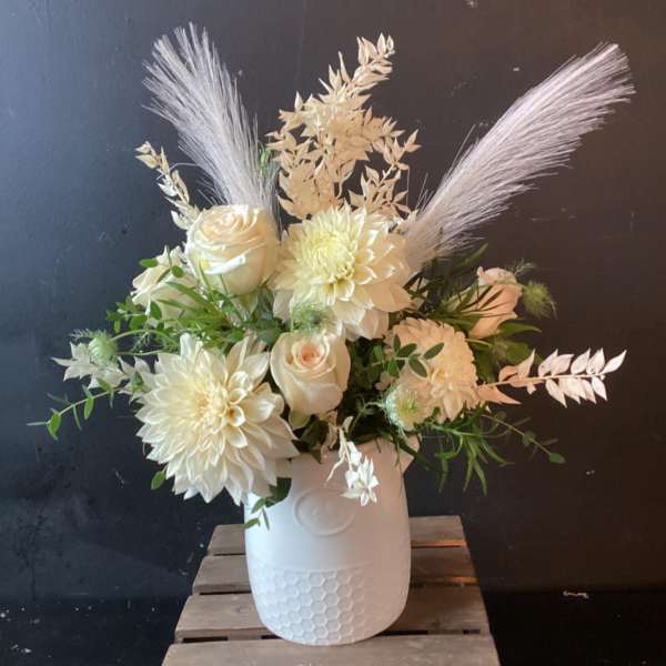 White floral arrangement in a textured white vase with feathery accents
