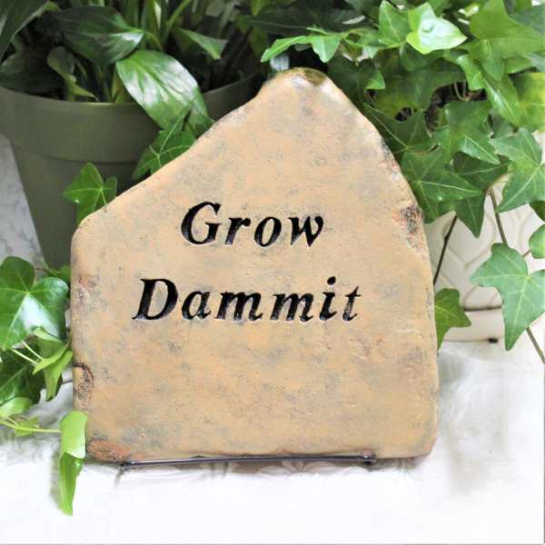 Stone sign reading "Grow Dammit" surrounded by potted ivy