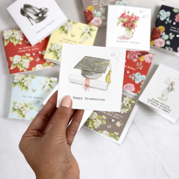 Hand holding a graduation card with a cap and diploma illustration