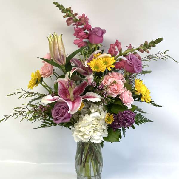 Mixed bouquet of lilies, roses, hydrangea, and daisies in a glass vase