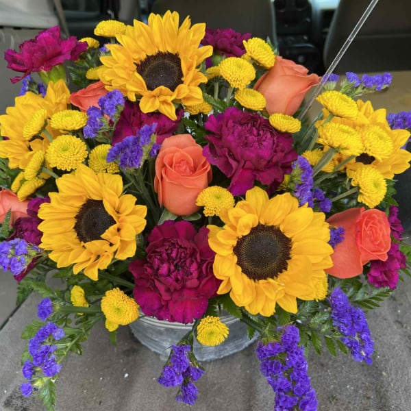 Bright mixed bouquet with sunflowers, roses, and purple blooms in a metal bucket