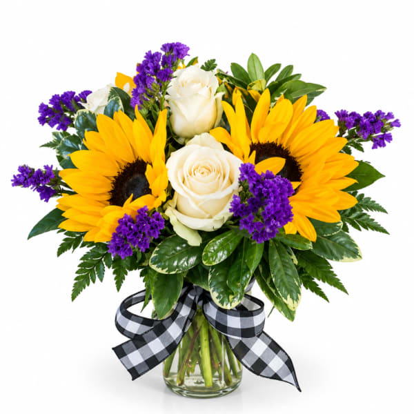 Bouquet of yellow sunflowers, white roses, and purple filler in a glass vase with a checkered ribbon
