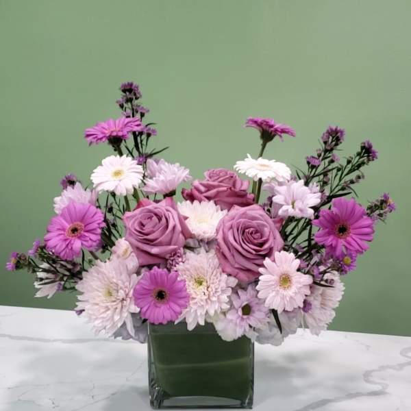 Pink and lavender roses with daisy-like flowers in a square glass vase