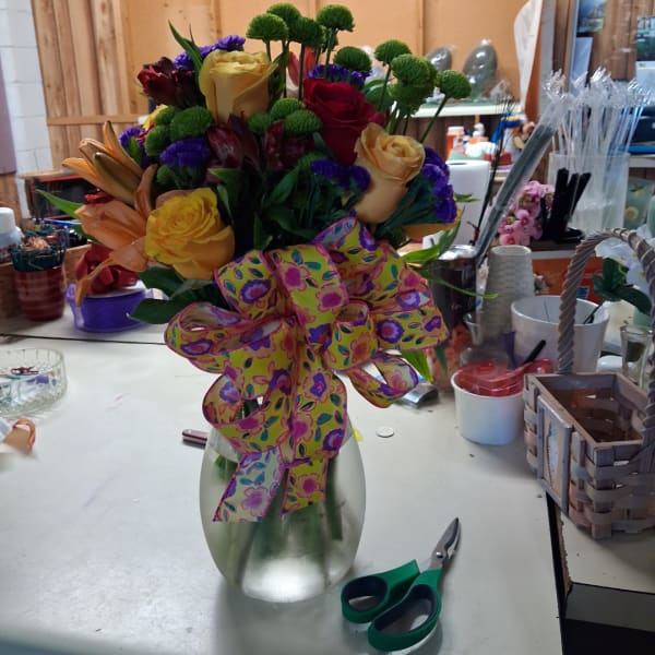 Mixed bouquet of roses and lilies in a glass vase with a patterned ribbon