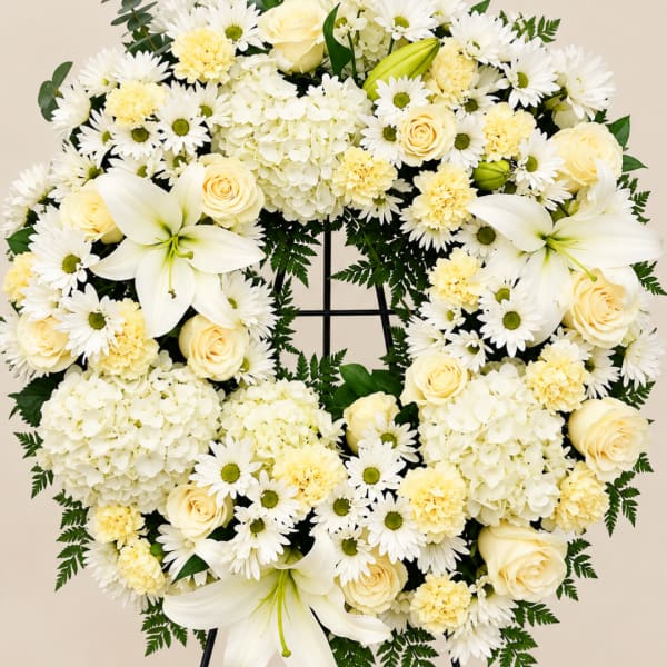 Heart-shaped white floral wreath with roses, daisies, lilies, and hydrangeas