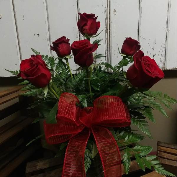 Red roses arranged in a glass vase with a large red ribbon.