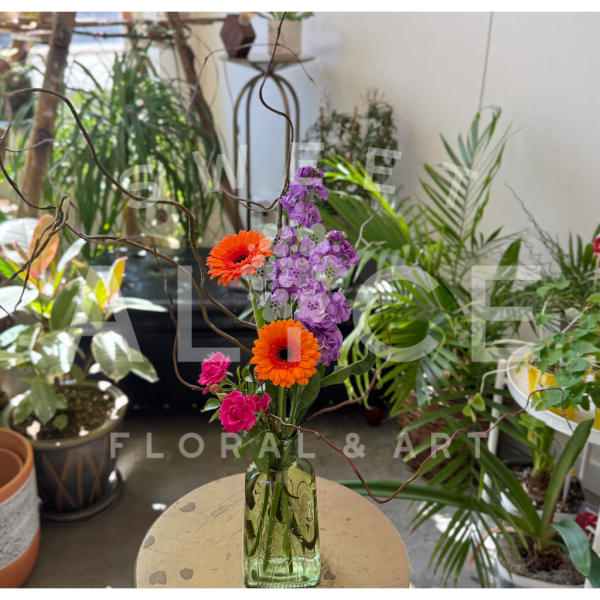 Orange and pink flowers in a green glass vase with curly branches