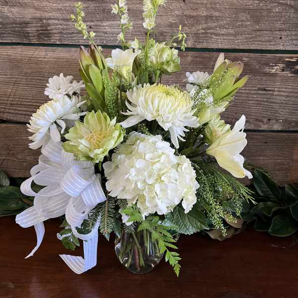 White floral arrangement in a clear glass vase with a white ribbon