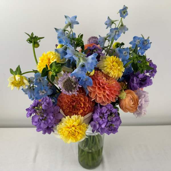 Mixed bouquet of blue, purple, yellow, and peach flowers in a glass vase
