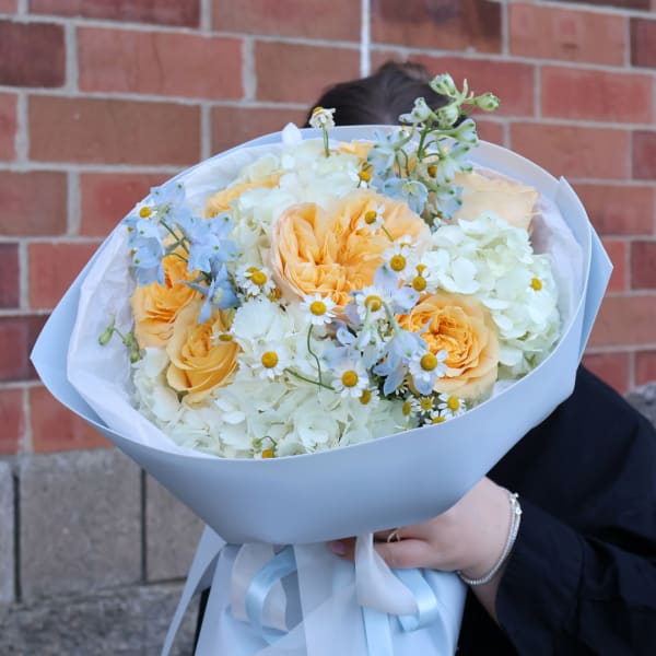 Bouquet of peach roses, white hydrangeas, and small daisy flowers wrapped in white paper