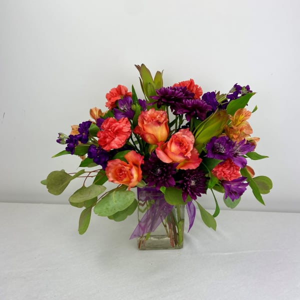 Mixed bouquet of purple, coral, and orange flowers in a glass vase