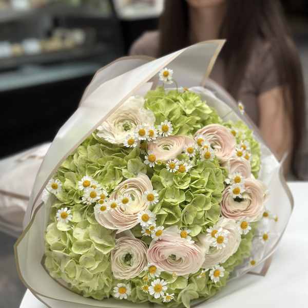 Bouquet of pale pink ranunculus and small white daisies in white wrap