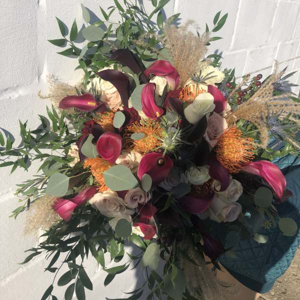 Large bouquet of burgundy calla lilies, cream roses, and orange protea with cascading greenery