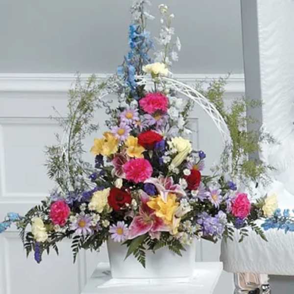Tall mixed floral arrangement in a white container with bright multicolored blooms
