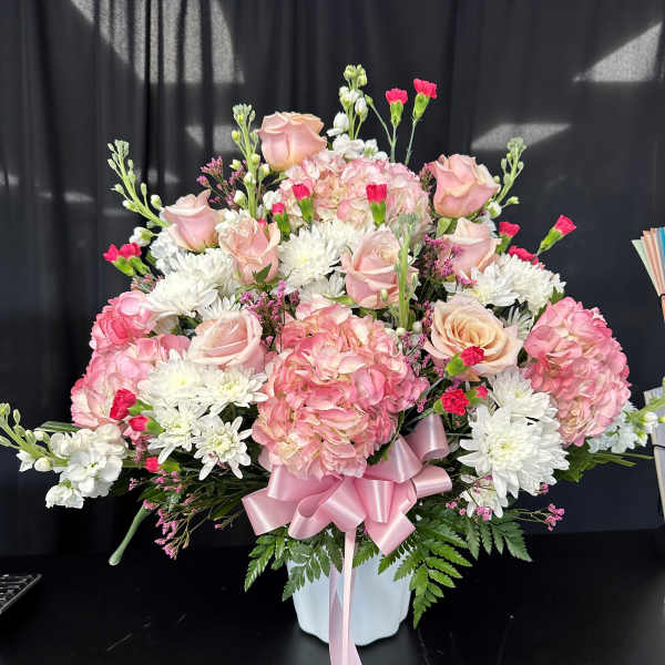 Pink roses and hydrangeas in a white vase with a pink ribbon