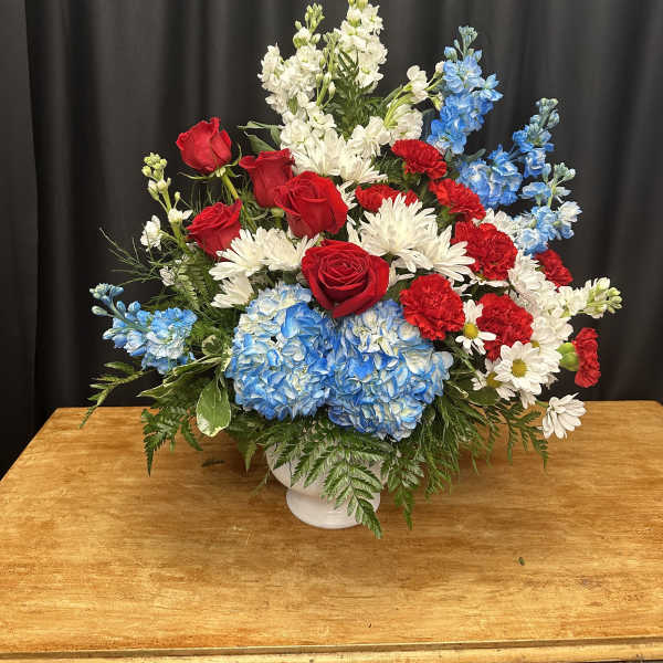 Red roses, blue hydrangeas, and white daisies in a white vase