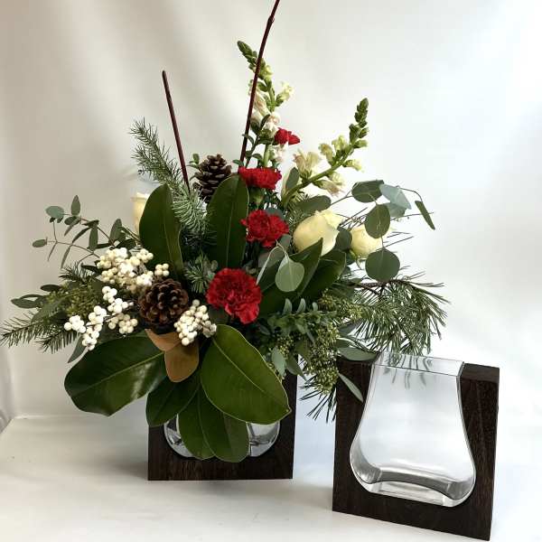 Holiday floral arrangement with red carnations, white blooms, pinecones, and greenery in a glass vase