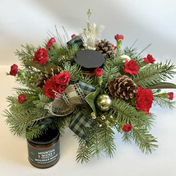 Holiday greenery arrangement with red carnations and pinecones beside a candle jar