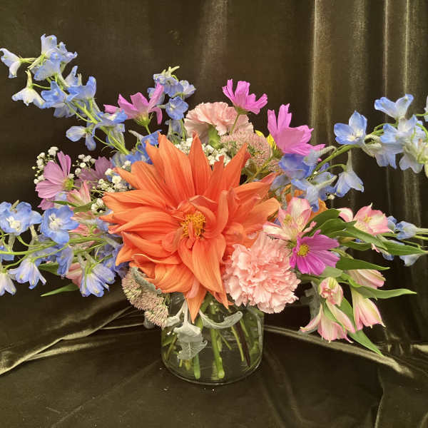 Colorful mixed bouquet in a clear glass vase with orange, pink, and blue flowers