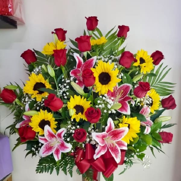 Large bouquet of red roses, yellow sunflowers, and pink lilies in a silver vase