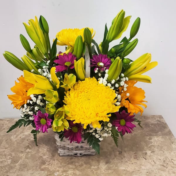 Basket arrangement of yellow lilies, chrysanthemums, and purple daisies