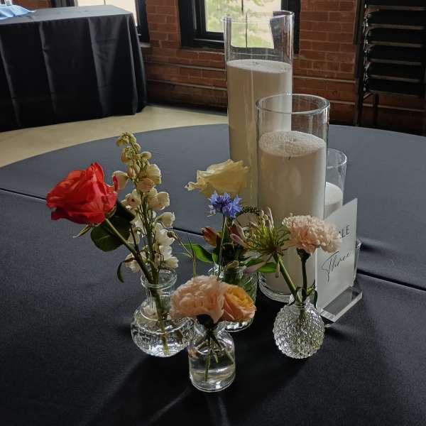 Small floral arrangements in glass vases around tall pillar candles on a table
