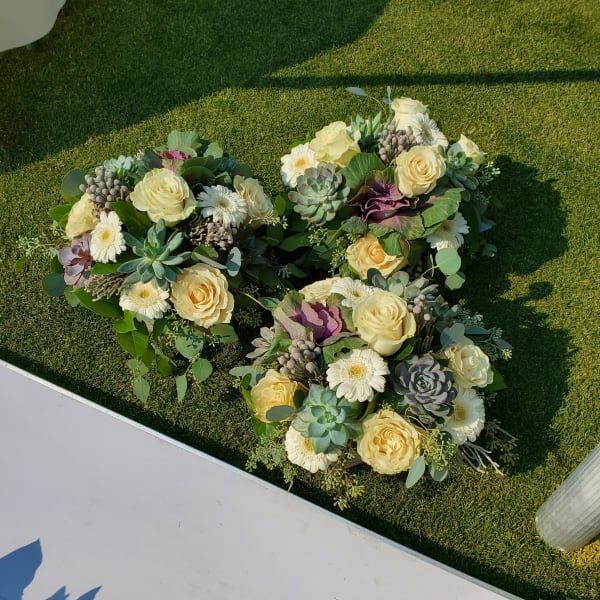 Heart-shaped floral arrangement with cream roses and white daisies on grass