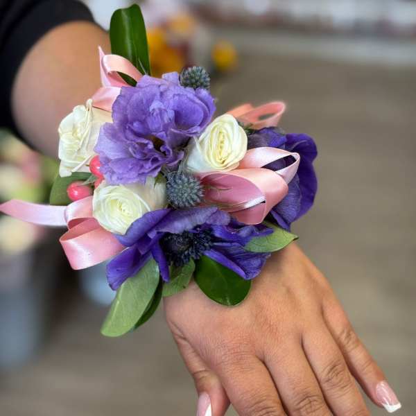 Purple and white wrist corsage with pink ribbon on a hand