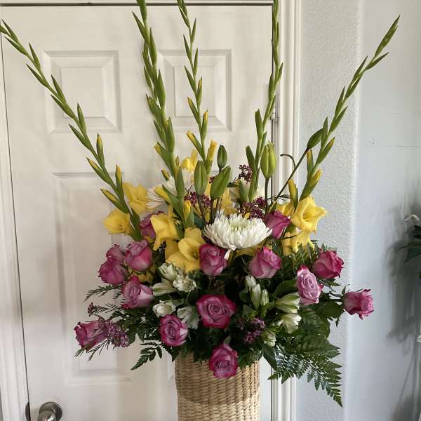 Tall mixed bouquet of pink and yellow flowers in a woven basket vase
