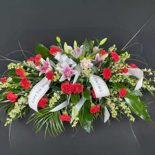 Sympathy spray with pink lilies, red carnations, and white ribbons