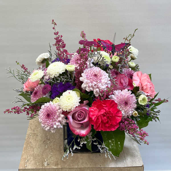 Mixed pink and white flower arrangement in a square vase with a butterfly decoration