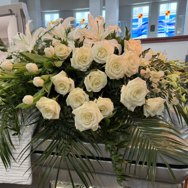 White roses and lilies arranged on a casket with greenery