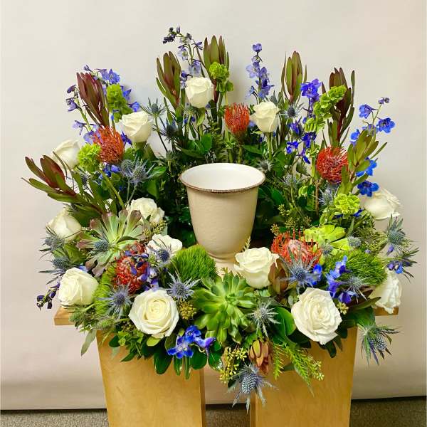 Large floral arrangement with white roses, blue flowers, and succulents in a cream urn