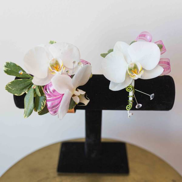 White orchid corsages with pink ribbon on a black display stand