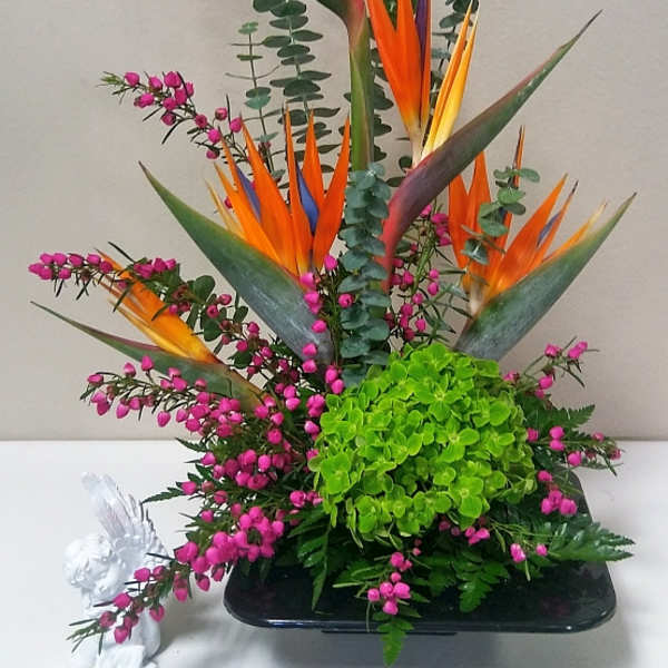 Tall tropical arrangement with orange bird of paradise and pink filler flowers in a black vase