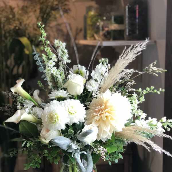 White floral arrangement in a clear glass vase with calla lilies and dahlias