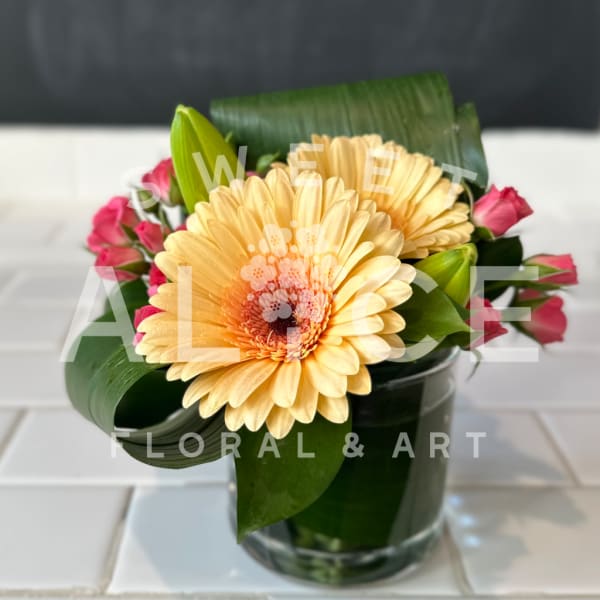 Yellow gerbera daisies with pink roses in a glass vase