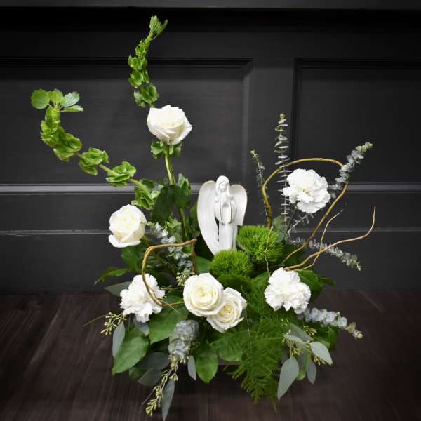 White roses and carnations arranged with greenery and a small angel figurine