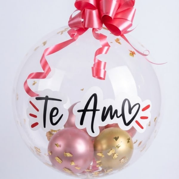 Clear balloon with pink ribbon, gold confetti, and "Te Amo" text