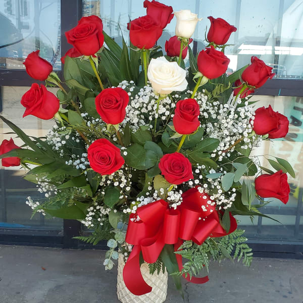 Tall bouquet of red and white roses in a cream vase with a red ribbon