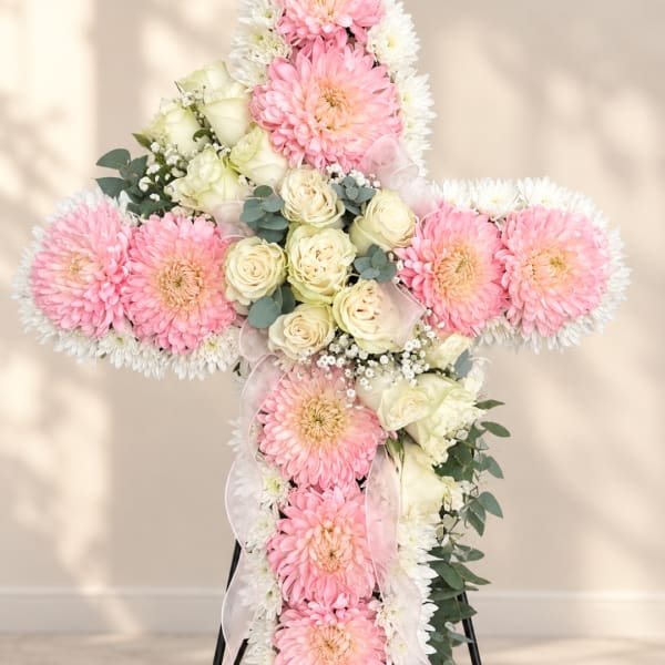 Cross-shaped floral arrangement with pink and white flowers and ribbon