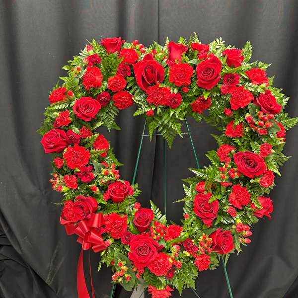 Heart-shaped red rose and carnation wreath on a stand with a red ribbon