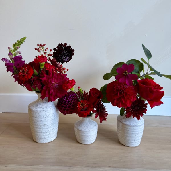 Three red and magenta flower arrangements in white ceramic vases