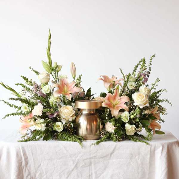 Floral centerpiece with lilies and roses around a gold urn
