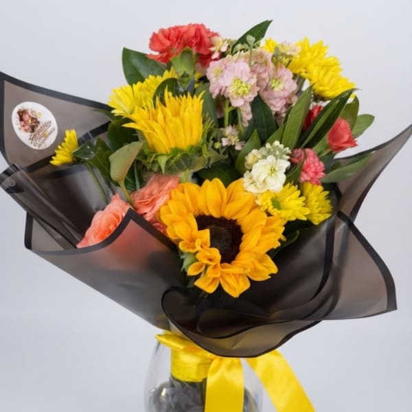 Bouquet with sunflowers, pink carnations, and yellow daisies in black wrap