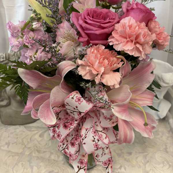 Pink roses, lilies, and carnations in a glass vase with a floral ribbon