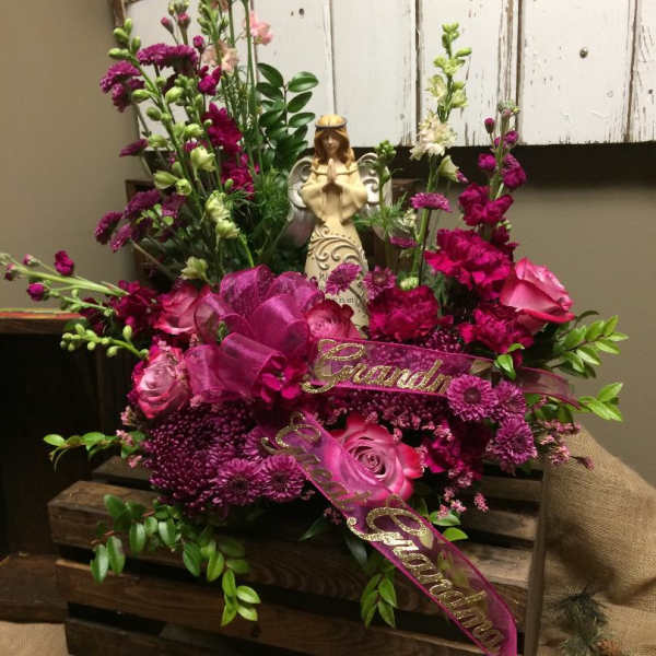 Pink and magenta floral arrangement with a figurine and ribbon in a wooden crate